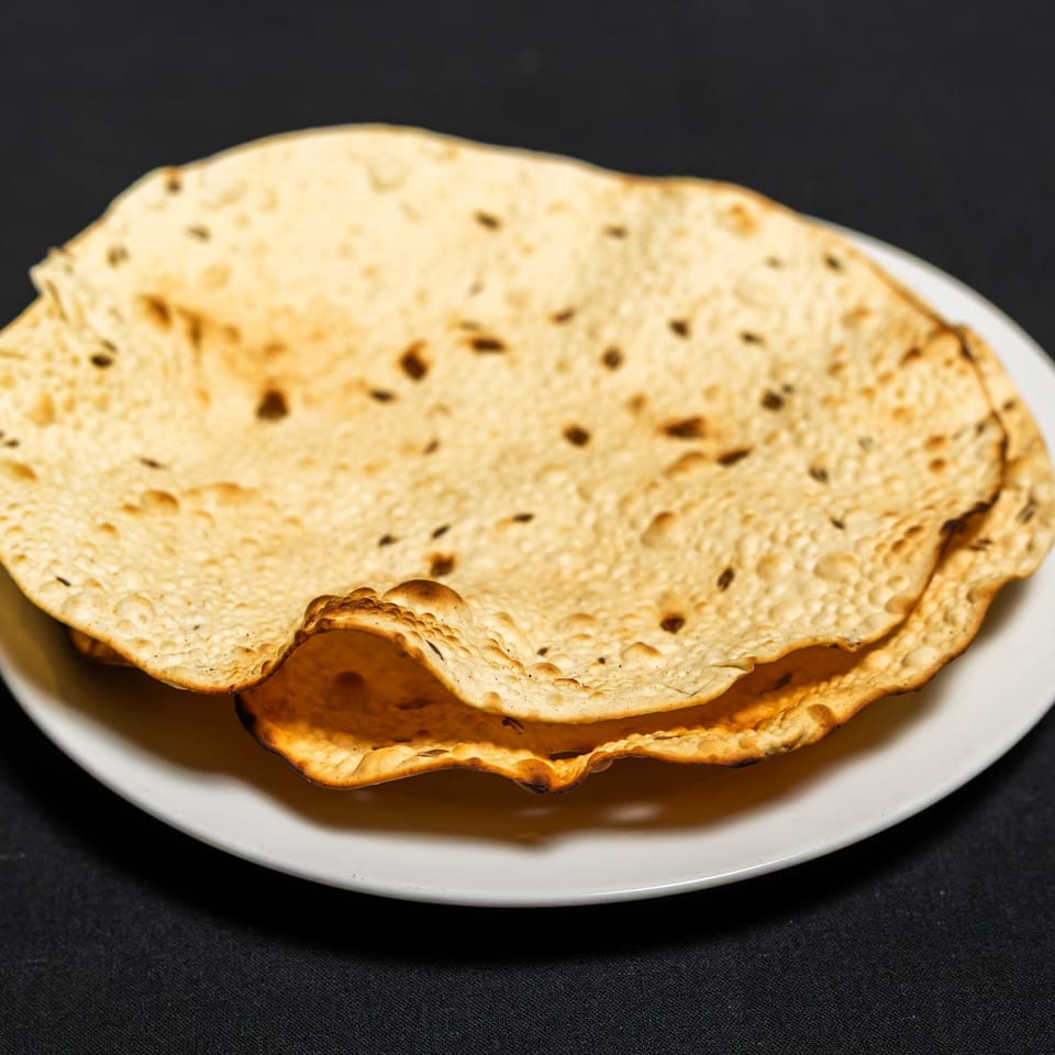 Crispy Indian papadums with spices, served on a white plate at Grand Dhaba.