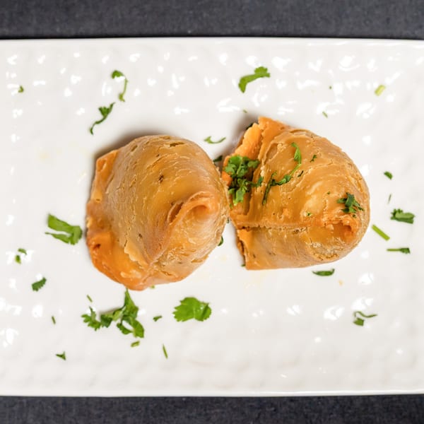 Two golden-brown samosas, one split open, garnished with fresh cilantro on a white plate.