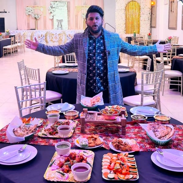 A man stands with arms outstretched behind a table laden with Indian dishes at Grand Dhaba.