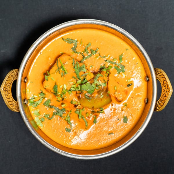 Overhead view of a Grand Dhaba Indian curry dish with bell peppers and cilantro in a metal bowl.