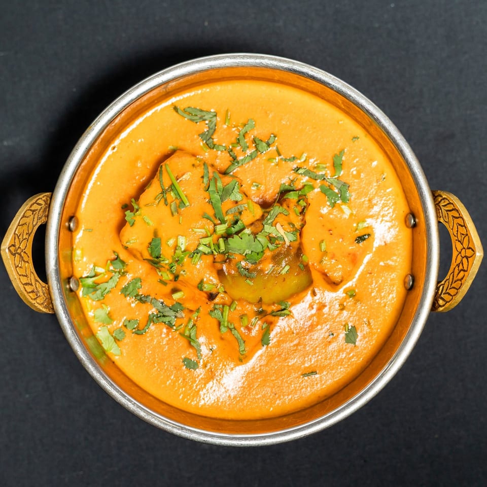 Overhead view of a Grand Dhaba Indian curry dish with bell peppers and cilantro in a metal bowl.