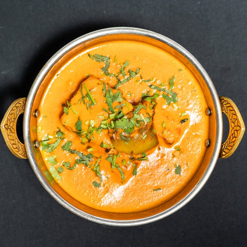 Overhead view of a Grand Dhaba Indian curry dish with bell peppers and cilantro in a metal bowl.