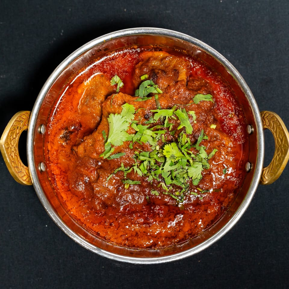 Grand Dhaba's Indian curry, a rich red stew with meat and fresh cilantro, in a metal serving bowl.