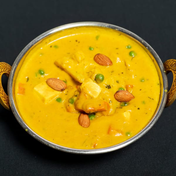 A vibrant yellow Indian curry with paneer, peas, and almonds in a metal bowl.