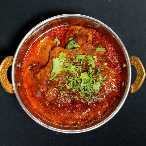 Grand Dhaba's Indian curry, a rich red stew with meat and fresh cilantro in a metal bowl.