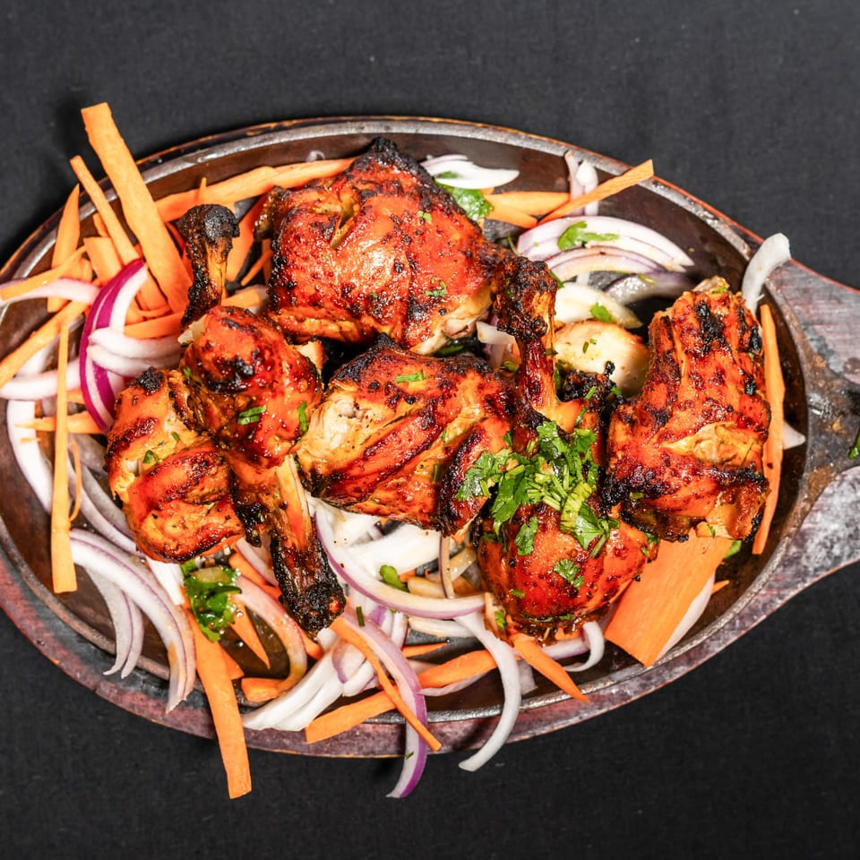Grand Dhaba's Indian tandoori chicken drumsticks, garnished with fresh cilantro, onions, and carrots.