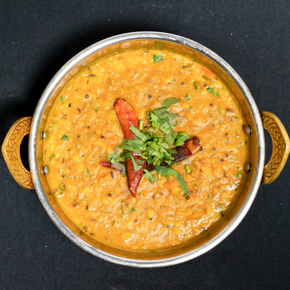 Grand Dhaba's Indian dal, garnished with red chilies and fresh cilantro in a metal bowl.