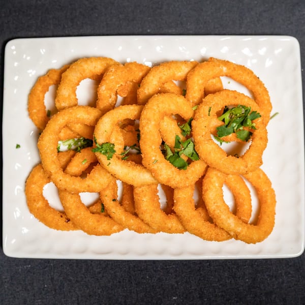 Crispy golden onion rings, garnished with fresh green herbs, served on a white rectangular plate.