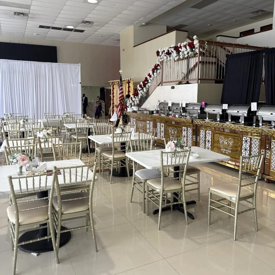 Grand Dhaba's spacious dining area with tables, chairs, a buffet line, and a floral-decorated staircase.