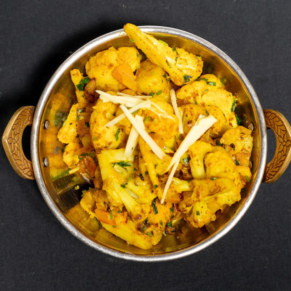 Grand Dhaba's Aloo Gobi, a vibrant Indian dish with cauliflower and potatoes, garnished with ginger.