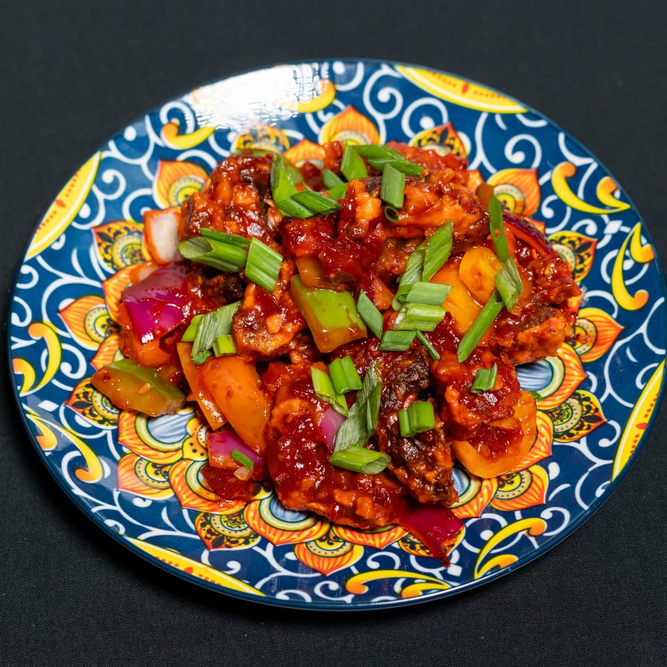 Grand Dhaba's Indian chili chicken, garnished with chopped scallions, bell peppers, and onions on a vibrant plate.