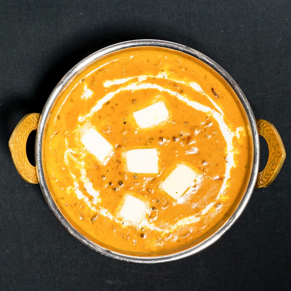 Overhead view of Grand Dhaba's creamy orange Dal Makhani, topped with white butter, in a silver bowl.