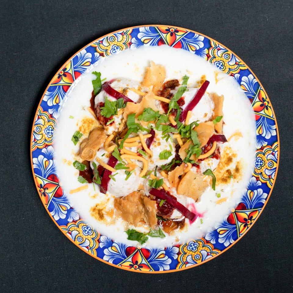 Dahi Bhalla, an Indian dish, with yogurt, chutneys, spices, sev, and cilantro on a colorful plate.