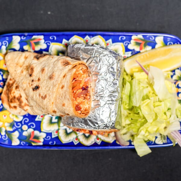 Two Indian burritos, one unwrapped, with lettuce and a lemon wedge on a blue patterned plate.
