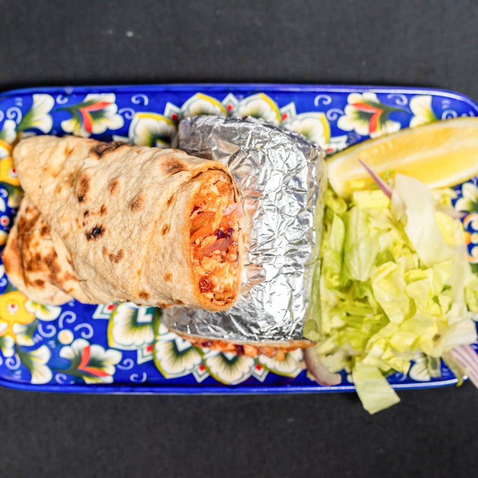 Two Indian burritos, one unwrapped, with lettuce and a lemon wedge on a blue patterned plate.